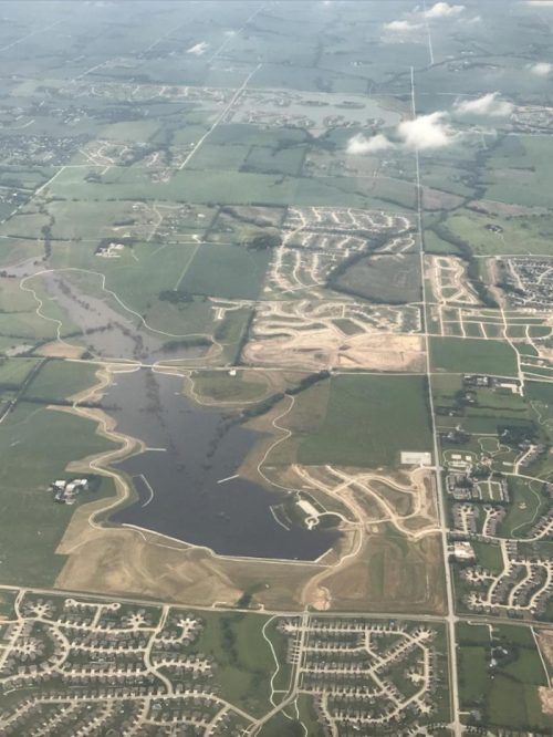 Aerial view of a rural landscape featuring fields, a large pond, and developing residential areas.