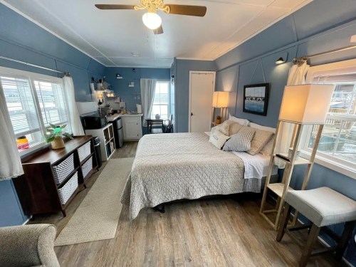 Cozy bedroom with a queen bed, kitchenette, and large windows, featuring light blue walls and modern decor.