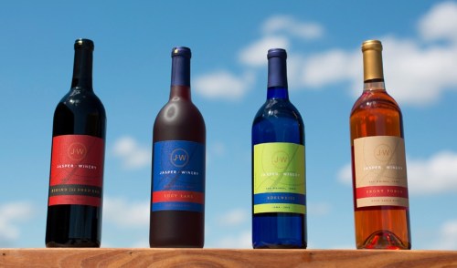 Four bottles of Jasper Winery wine in various colors, displayed against a blue sky.
