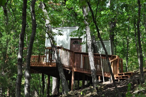 A treehouse nestled among trees, featuring a wooden deck and a door, surrounded by lush greenery.