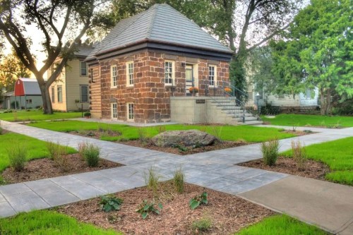 A small stone house with a sloped roof surrounded by landscaped paths and greenery in a park-like setting.