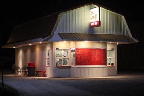 A brightly lit food stand at night, featuring a red menu board and outdoor seating.