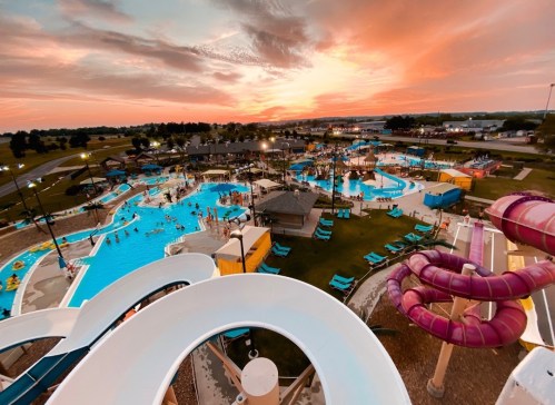Aerial view of a vibrant water park at sunset, featuring pools, slides, and people enjoying the attractions.