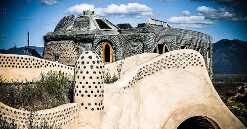 A unique, textured building with rounded shapes and dotted patterns, set against a mountainous landscape and blue sky.