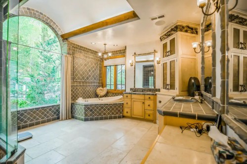 Spacious bathroom with large windows, a soaking tub, and elegant tile work. Natural light fills the room.
