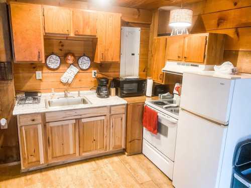 Cozy wooden kitchen with a sink, stove, microwave, and refrigerator, featuring rustic cabinets and warm lighting.