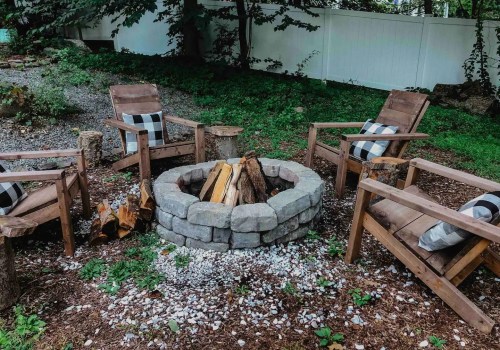 A cozy outdoor fire pit surrounded by wooden chairs and a stone circle, set in a green, wooded area.