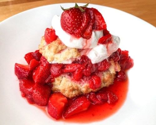 A delicious dessert featuring layers of biscuit, whipped cream, and fresh strawberries in a sweet sauce.