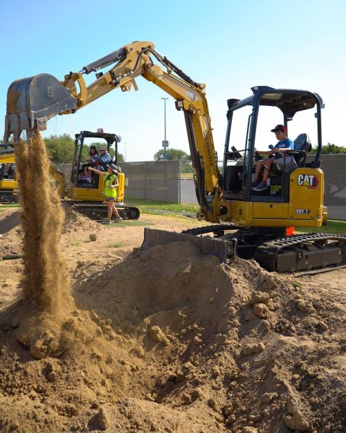 A yellow excavator digs into the ground, with sand pouring from its bucket, while another excavator operates nearby.