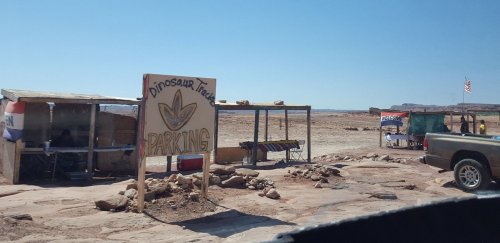 Sign for "Dinosaur Tracks Parking" at a remote location with a clear blue sky and desert landscape.