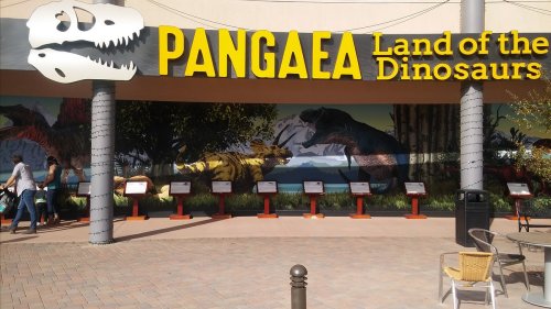 Sign for "Pangaea: Land of the Dinosaurs" with dinosaur murals and informational displays in a vibrant outdoor setting.