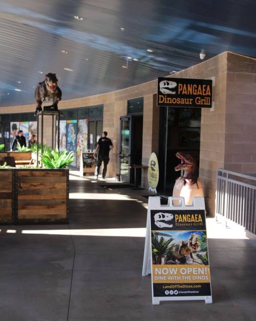 Sign for Pangaea Dinosaur Grill, featuring a T-Rex statue and a banner announcing it's now open.