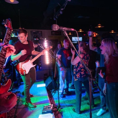 A lively band performs on stage while an enthusiastic crowd dances and enjoys the music in a vibrant venue.