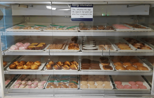A display case filled with various baked goods, including cookies and pastries, with an allergy information sign above.