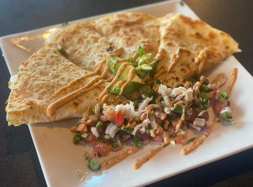 A plate of quesadillas drizzled with sauce, served with a side of fresh salsa and chopped vegetables.