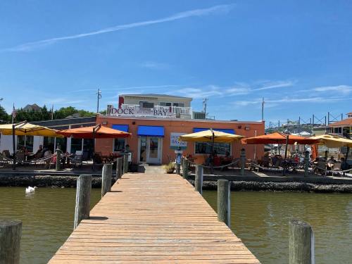 A waterfront restaurant with colorful umbrellas, a wooden dock, and a clear blue sky.
