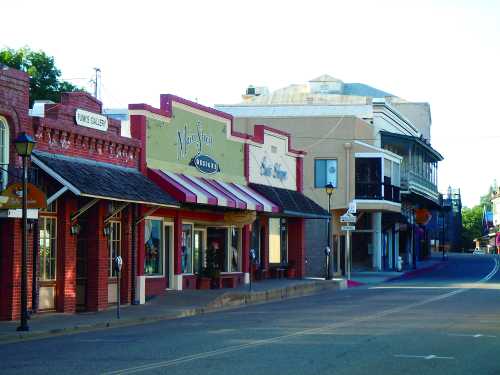 Quaint street lined with shops and galleries, featuring colorful storefronts and a clear blue sky.