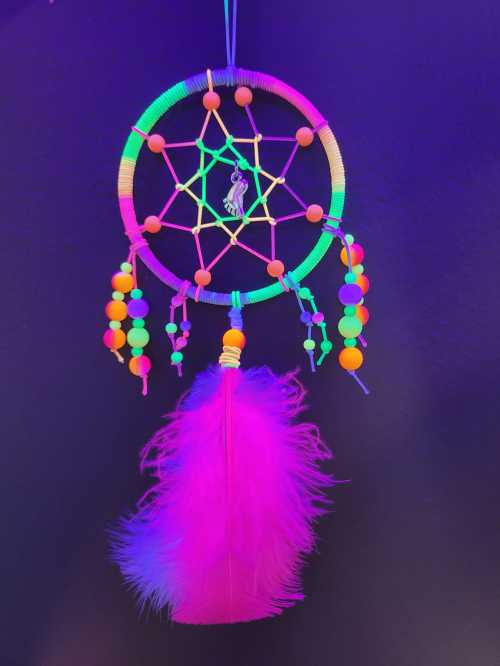 A colorful dreamcatcher with neon beads and a pink feather, hanging against a dark background.