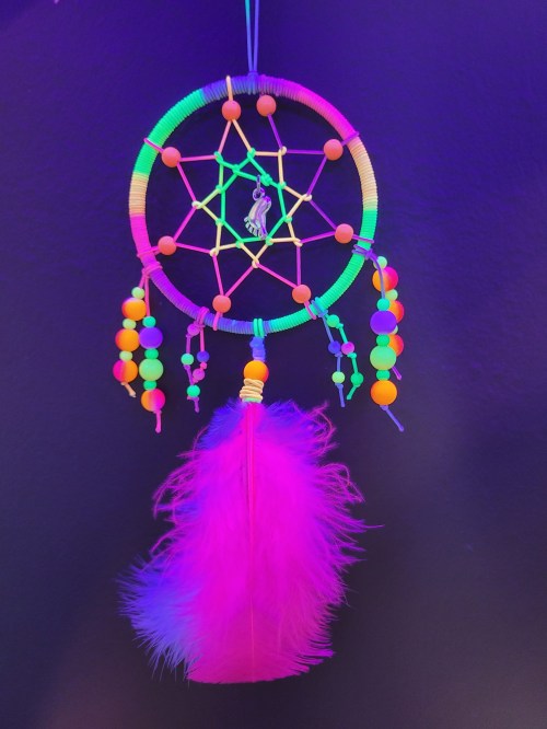 A colorful dreamcatcher with neon beads and a pink feather, hanging against a dark background.