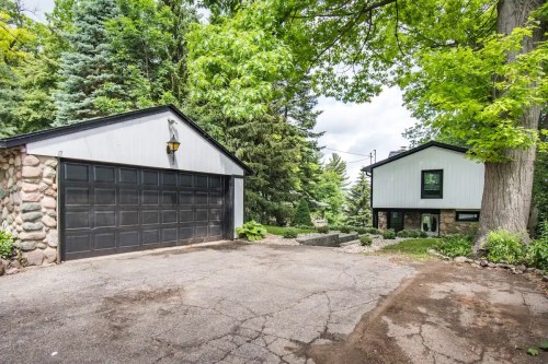 A modern house with a stone garage, surrounded by lush green trees and a gravel driveway.