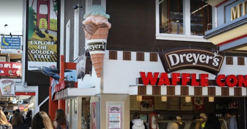 A Dreyer's ice cream shop with a large ice cream cone sign, bustling with people in a vibrant street setting.