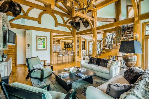 Cozy living room with wooden beams, plush furniture, and a staircase leading to an upper level. Decorated with rustic accents.