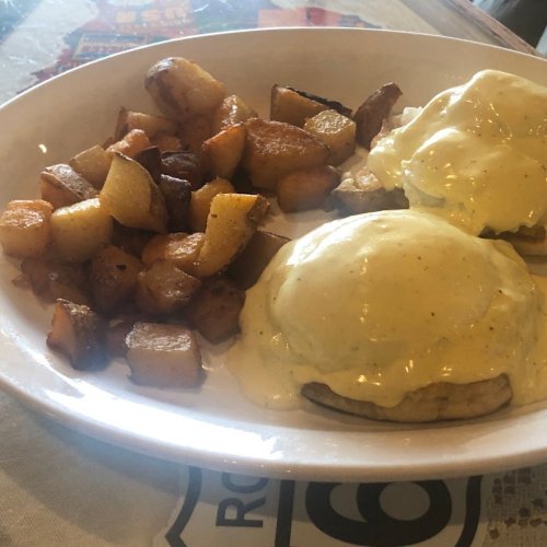 A plate of eggs Benedict with hollandaise sauce and crispy roasted potatoes on the side.