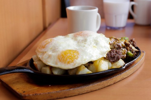 A sizzling skillet with potatoes, ground beef, and two sunny-side-up eggs, served on a wooden platter.