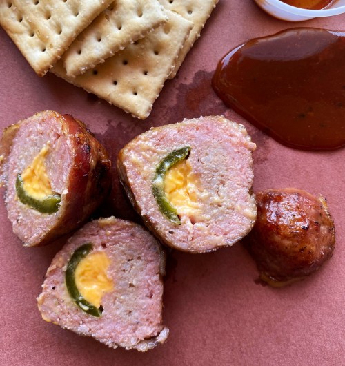 Sliced meatloaf stuffed with cheese and jalapeños, served with crackers and dipping sauce on a brown background.