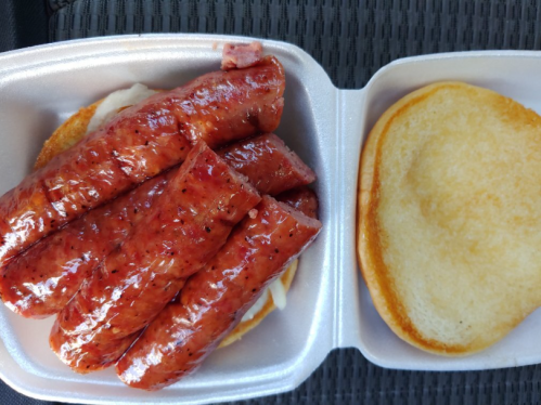 A container with a sandwich featuring several grilled sausage links on a bun, with a plain bun beside it.