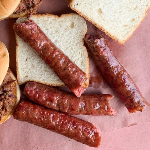 Close-up of sliced sausage links on white bread, with some sausage pieces placed beside the bread.