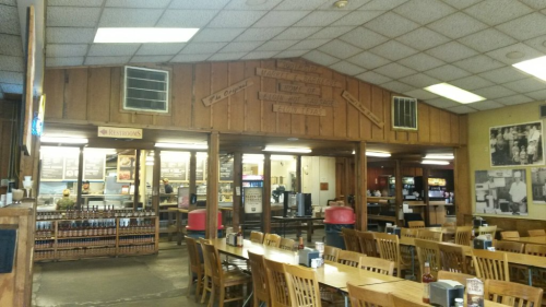 Interior of a rustic restaurant with wooden decor, tables, and a counter displaying menu items.