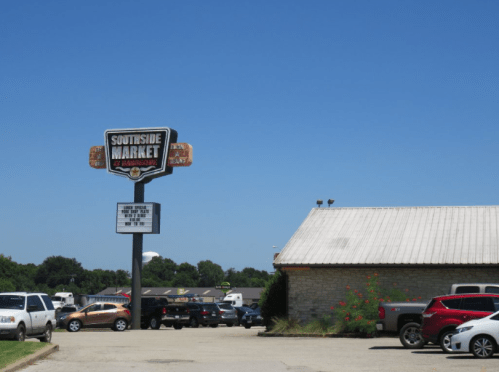A sign for Southside Market stands outside a building, with parked cars and a clear blue sky in the background.