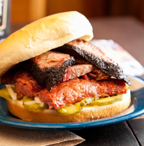 A hearty sandwich stacked with various meats, pickles, and onions, served on a soft bun on a blue plate.