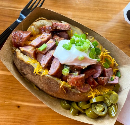 Baked potato topped with chopped sausage, cheese, green onions, a dollop of sour cream, and sliced jalapeños.