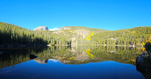 A serene mountain lake surrounded by rugged cliffs and trees under a clear blue sky.