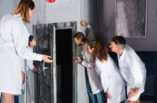 A group of five people in lab coats curiously peering through a door in a mysterious room.