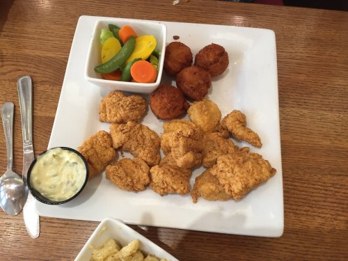 A plate with fried chicken pieces, hushpuppies, a bowl of mixed vegetables, and a small cup of dipping sauce.