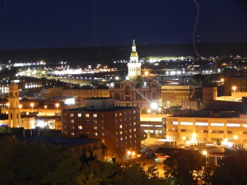 Nighttime cityscape featuring illuminated buildings and a clock tower against a dark sky.