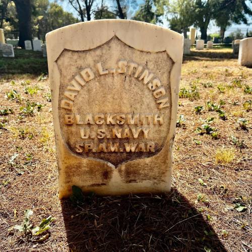 Gravestone of David L. Stinson, Blacksmith, U.S. Navy, Spanish-American War, in a cemetery with grass and trees.