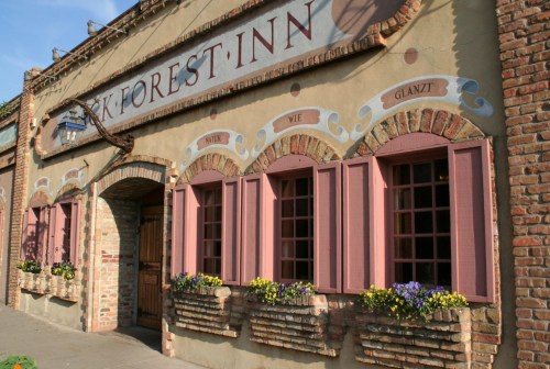 A charming inn with a brick facade, pink window shutters, and flower boxes, featuring decorative signage above the entrance.