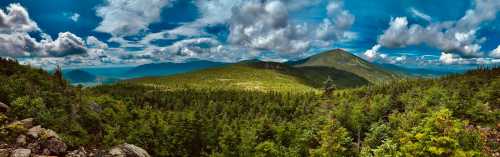 A panoramic view of lush green mountains under a bright blue sky with fluffy clouds.