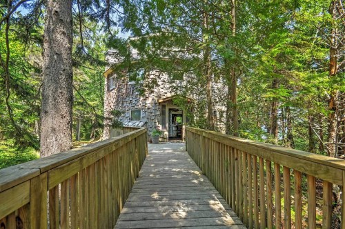 A wooden walkway leads to a rustic house surrounded by trees in a serene forest setting.