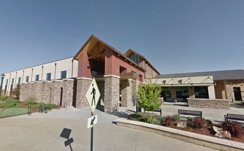 A modern building with a stone facade and large windows, featuring a landscaped entrance and pedestrian crossing sign.