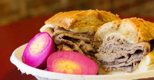A close-up of a sandwich filled with sliced beef, served with pink pickled onions on the side.