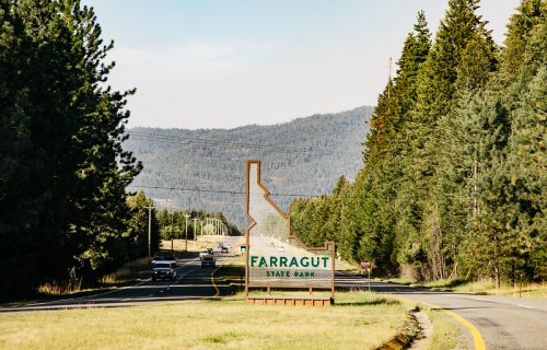 Sign for Farragut State Park along a winding road, surrounded by trees and mountains in the background.