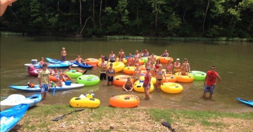 A group of people in colorful inner tubes enjoying a sunny day on a river, surrounded by trees and water.