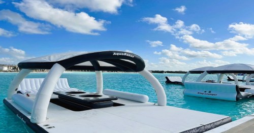 Floating lounge chairs on a turquoise sea under a blue sky with fluffy clouds.