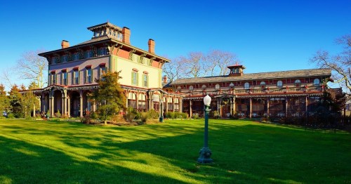 Historic mansion with colorful architecture, surrounded by green lawns and trees under a clear blue sky.
