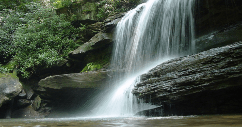 A serene waterfall cascading over rocky cliffs into a calm pool, surrounded by lush greenery.